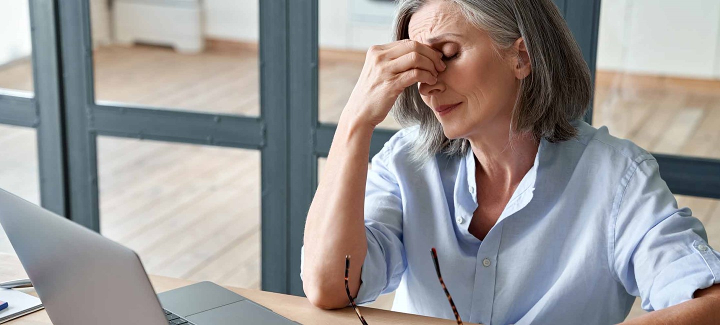 Older woman sitting at a desk with a laptop, having a headache
